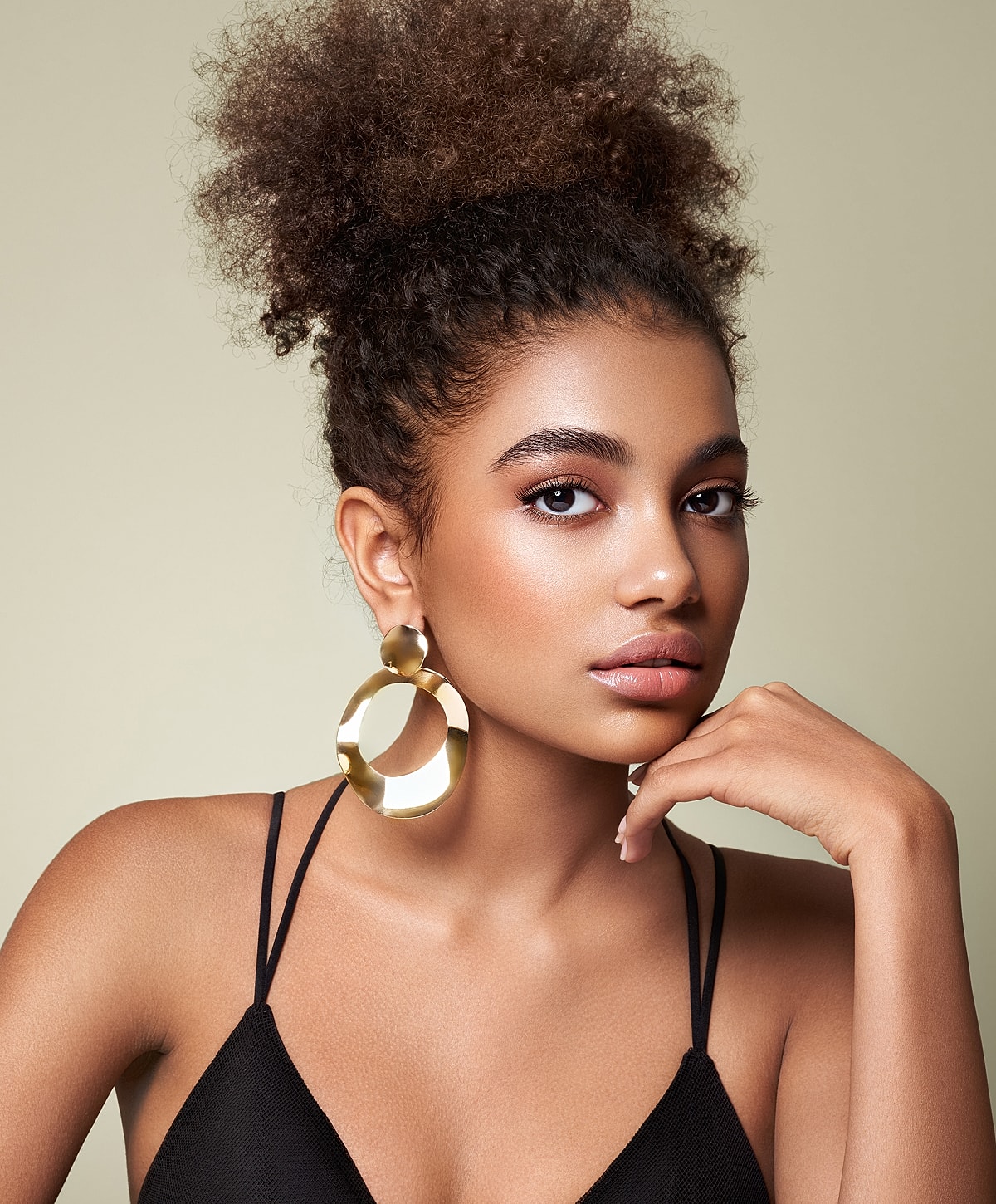Model with curly hair and bold earrings.